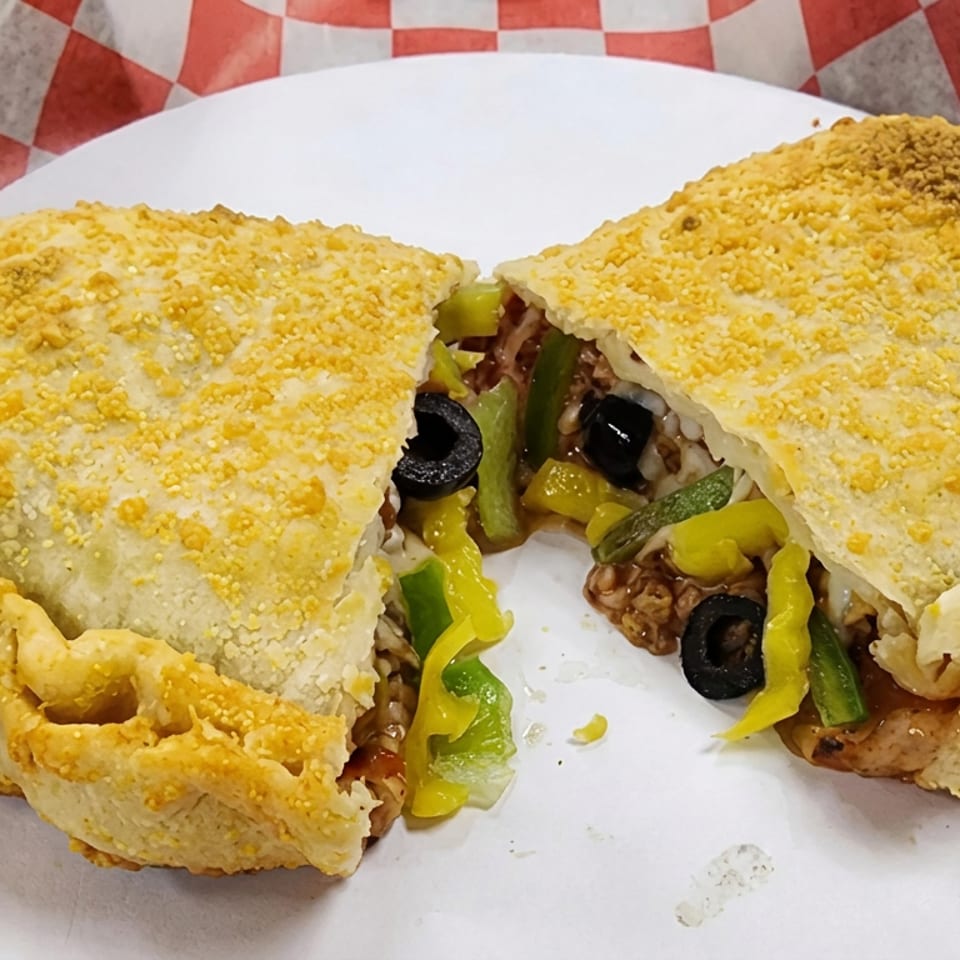 Sliced baked calzone filled with peppers, black olives, mushrooms, and melted cheese on a white plate.