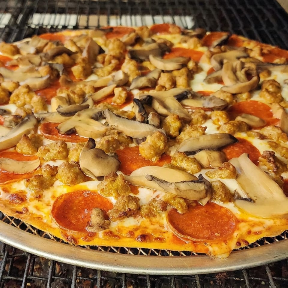 Large pepperoni pizza topped with mushrooms and sausage on a metal pan inside a commercial oven.